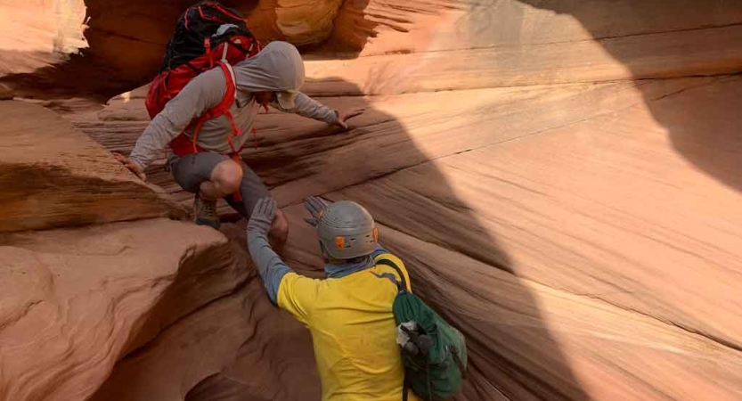 One person helps another navigate a short drop into a canyon.